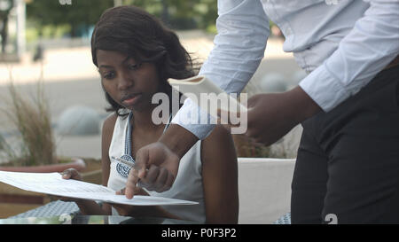Schöne afro-amerikanische Frau, die Bestellungen aus dem Menü im Restaurant und zu entscheiden, was zu Essen Stockfoto