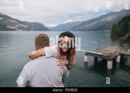 Rückansicht der Mann, der glückliche junge Frau in Sonnenbrille in der Nähe von Majestic Mountain Lake in Bern, Schweiz Stockfoto