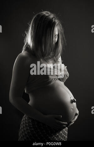 Studio Portrait der schwangeren Frau mit Warnton Bell, berühren Bauch, Schwarz und Weiß Stockfoto