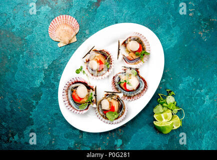 Raw geöffnet Schalentiere Jakobsmuscheln auf weiße Platte mit Zitrone und weißen Wein serviert, Türkis Hintergrund. Ansicht von oben. Meeresfrüchte Konzept. Stockfoto