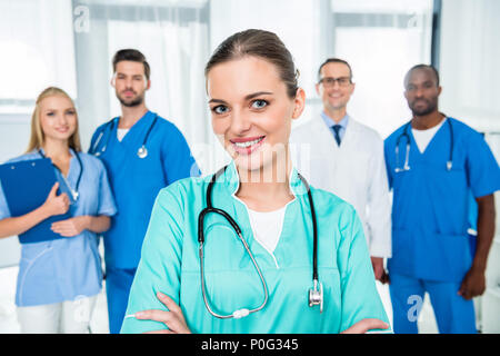 Junge attraktive Krankenschwester mit verschränkten Armen mit Kollegen gemeinsam auf Hintergrund Stockfoto