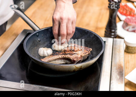 Zugeschnittenes Bild von Chef, Knoblauch braten Fleisch Stockfoto