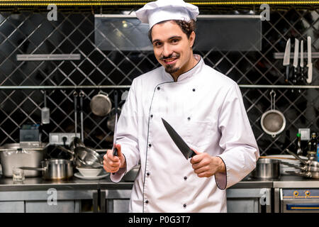 Lächelnd Küchenchef stehend mit Messern in der Küche Stockfoto