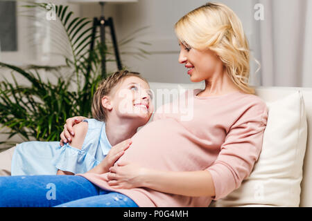 Porträt der lächelnde Mädchen berühren schwangere Bauch im Sitzen auf dem Sofa Stockfoto