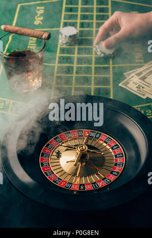 Smoke over female hand placing a bet on table with roulette Stockfoto