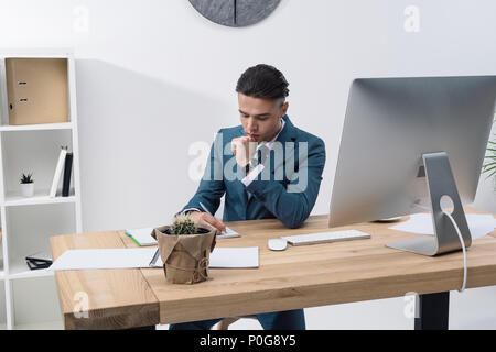 Konzentrierte junge Unternehmer schreiben in Notebook und gleichzeitig am Tisch arbeiten mit Desktop Computer Stockfoto