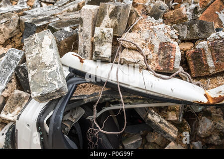 Gebrochen weißes Fahrzeug mit alten grauen Ziegeln aus zerstörten Mauer begraben. Detail. Versicherung Konzept. Stockfoto