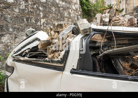 Gebrochen weißes Fahrzeug mit alten grauen Ziegeln aus zerstörten Mauer begraben. Detail. Versicherung Konzept. Stockfoto