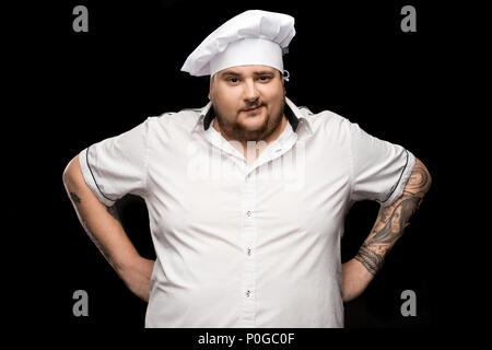 Professionelle junge Küchenchef in weißen Hut posiert isoliert auf Schwarz Stockfoto