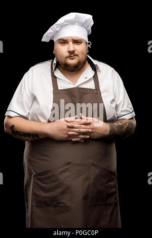 Professionelle junge Küchenchef in Hut und Schürze auf Schwarz isoliert Stockfoto