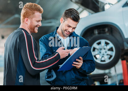 Junge automechanic zeigt einen lächelnden Client eine Zwischenablage an eine Reparaturwerkstatt. Stockfoto