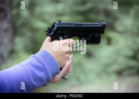 Frau schießt aus Luftgewehr Pistole (schwarz Air Gun) im Wald. Hände und Arme sichtbar, verschiedene Kamerawinkel Stockfoto