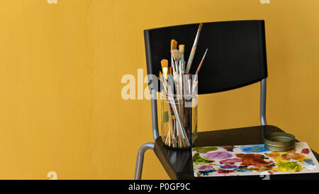 Werkzeuge der Künstler. Pinsel und Palette mit Ölfarben, jar mit Lösungsmittel stehen auf einen Stuhl. Stockfoto