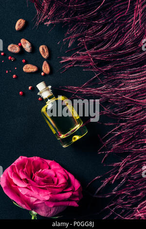 Blick von oben auf die Flasche Parfüm mit roter Feder und rose bud auf Schwarz Stockfoto