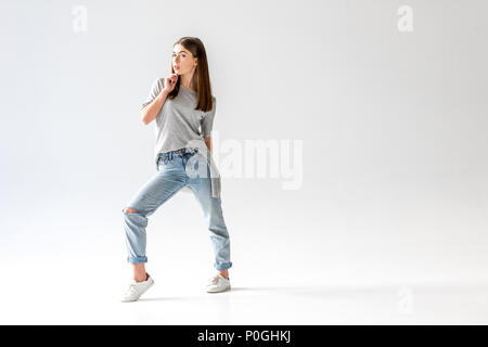 Junge stilvolle Frau, die in Jeans und T-Shirt grau an Kamera suchen, isoliert auf weißem Stockfoto