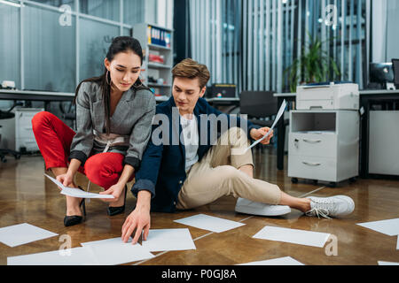 Young Business Partner Schreibarbeit zu tun, während auf dem Boden im Büro sitzen Stockfoto