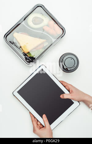 Zugeschnittenes Bild der Frau mit Tablet am Tisch mit Essen in Lunch Box isoliert auf weißem Stockfoto