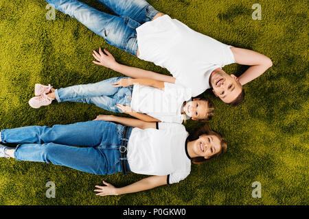 Ansicht von oben, die glückliche Familie in ähnliche Kleidung liegen auf grünen Rasen Stockfoto