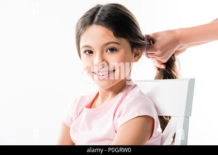 Zugeschnittenes Bild von Mutter binden Töchter lange Haare im Zopf isoliert auf weißem Stockfoto