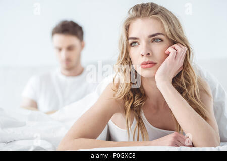 Junge nachdenkliche Frau im Bett liegend mit Freund hinter Stockfoto