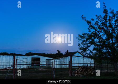 Full moon over rural barn during evening, dusk, twilight, blue hour, serene landscape, outbuilding, night, farmyard, moonrise, Stockfoto