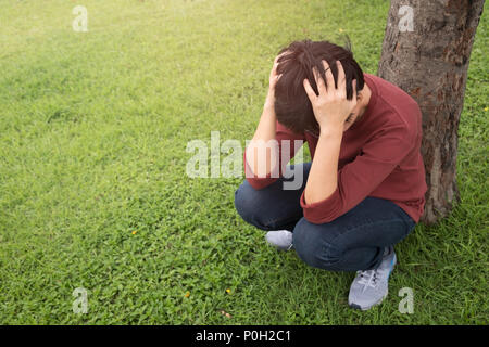 Eine Person trägt ein rotes Hemd, packt seine Kopf mit Stress im Garten bei Sonnenuntergang. Psychische Gesundheit, Depression Konzept. Stockfoto