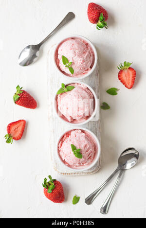 Erdbeereis und frische Erdbeeren auf weißem Hintergrund, Ansicht von oben. Drei Becher Erdbeereis, gesunden Sommer Nachtisch. Stockfoto