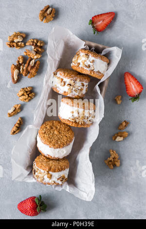 Eis-Sandwiches mit Muttern und Vollkorn Cookies. Hausgemachtes Vanilleeis Sandwiches auf grauem Beton Hintergrund. Stockfoto