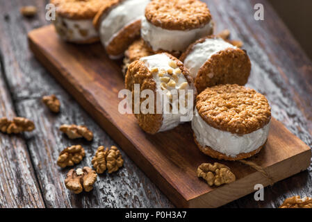 Eis-Sandwiches mit Muttern und Vollkorn Cookies. Hausgemachtes Vanilleeis Sandwiches auf dunklem Hintergrund. Stockfoto