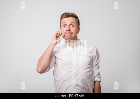 Portrait von gutaussehenden jungen Mann im weißen Hemd seinen Mund schließen, ist er gezwungen, geheim zu halten, nicht jedermann zu erzählen. Stockfoto