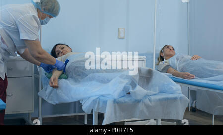 Zwei weibliche Patienten auf tropft liegt auf Betten im Krankenhaus durch zwei Ärzte geprüft werden Stockfoto