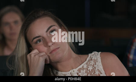 Schöne Frau auf der Suche extrem langweilig allein Witting in einem leeren Kinosaal beobachten ein langweiliger Film Stockfoto