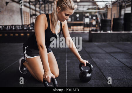 Junge blonde Frau in Workoutkleidung allein Trainieren mit Gewichten in einer Turnhalle konzentriert Stockfoto