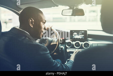 Rückspiegel eines jungen afrikanischen Geschäftsmann ändern Radiosender, während Sie durch die Straßen der Stadt in seinem Auto fahren Stockfoto