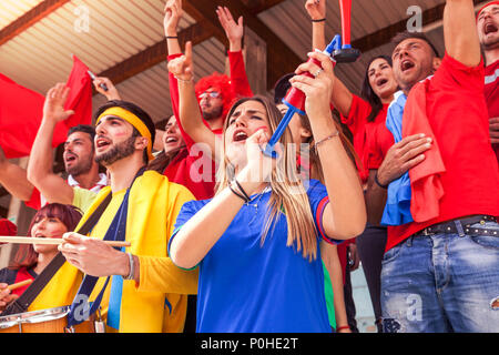 Gruppe von Fans in verschiedenen Farben beobachten ein sportliches Ereignis auf der Tribüne des Stadions gekleidet Stockfoto
