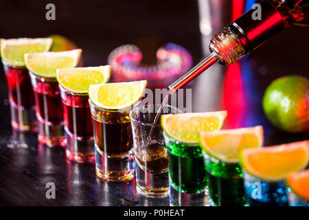 Barkeeper gießen alkoholisches Getränk in kleine Gläser an der Bar. Farbenfrohe Cocktails an der Bar. Farbenfrohe Aufnahmen im Club. Alkoholische Getränk in verschiedenen c Stockfoto