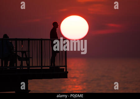 Aberystwyth Wales UK, Samstag, 09. Juni 2018 Deutschland Wetter: Die herrliche Sonne im orange sky Silhouetten Menschen genießen Sie einen Drink auf der viktorianischen Badeort Pier in Aberystwyth an der Westküste von Wales, am Ende eines Tages des heißen Sommer Sonnenschein Foto © Keith Morris/Alamy leben Nachrichten Stockfoto