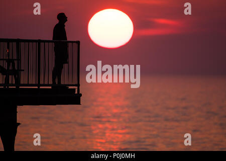 Aberystwyth Wales UK, Samstag, 09. Juni 2018 Deutschland Wetter: Die herrliche Sonne im orange sky Silhouetten Menschen genießen Sie einen Drink auf der viktorianischen Badeort Pier in Aberystwyth an der Westküste von Wales, am Ende eines Tages des heißen Sommer Sonnenschein Foto © Keith Morris/Alamy leben Nachrichten Stockfoto