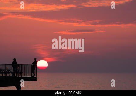 Aberystwyth Wales UK, Samstag, 09. Juni 2018 Deutschland Wetter: Die herrliche Sonne im orange sky Silhouetten Menschen genießen Sie einen Drink auf der viktorianischen Badeort Pier in Aberystwyth an der Westküste von Wales, am Ende eines Tages des heißen Sommer Sonnenschein Foto © Keith Morris/Alamy leben Nachrichten Stockfoto