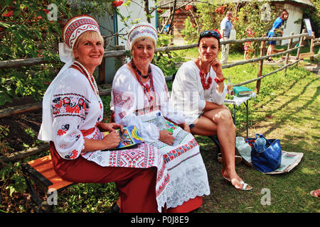 3 ukrainische Sängerinnen in bestickten Hemden sitzen auf der woonierten Bank am Holzzaun auf der Sorochintsi Agro Fair in der Poltava Region Ukraine. Stockfoto