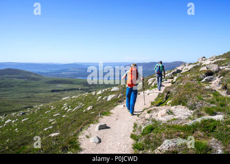 Zwei hillwalkers/Bergsteiger mit Stöcken und Rucksäcken absteigend Bergweg im Frühjahr im Cairngorms Nationalpark, Highland, Schottland Stockfoto