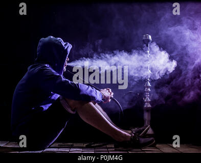 Ein Mann raucht eine Shisha auf schwarzem Hintergrund, schöne Beleuchtung Stockfoto