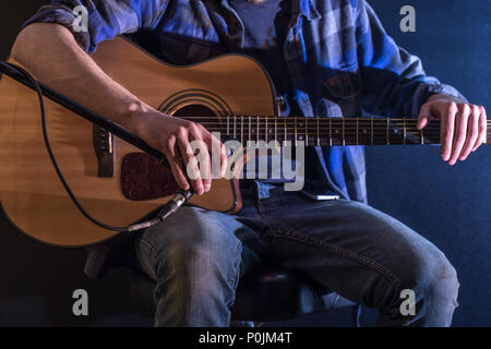 Mann spielt Akustische Gitarre auf einem schwarzen Hintergrund, die Musik Konzept, schöne Beleuchtung auf der Bühne Stockfoto