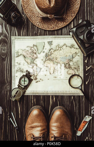 Blick von oben auf die Einstellung mit Strohhut, Karte, Schuhe, Kompass, Lupe und Fotokameras auf dunklen Holz- Oberfläche Stockfoto