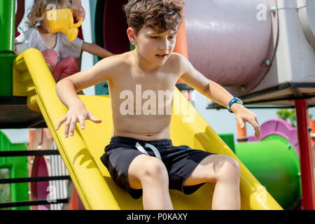 Junge vorsichtig spielen auf einem Kunststoff Folie in einer Kinderspielplatz Park Stockfoto