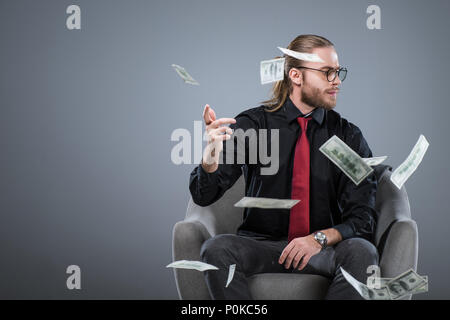 Unternehmer im Sessel sitzt, während Geld wegzuwerfen, isoliert auf Grau Stockfoto