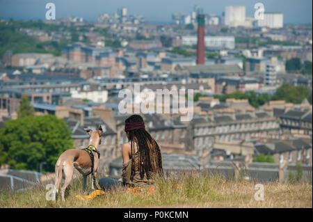 Eine sehr kühle, böhmische Mädchen sitzt in der langen Gras auf Carlton Hill an einem sonnigen Tag mit Edinburgh unter ihr und ihrem Hund Stockfoto