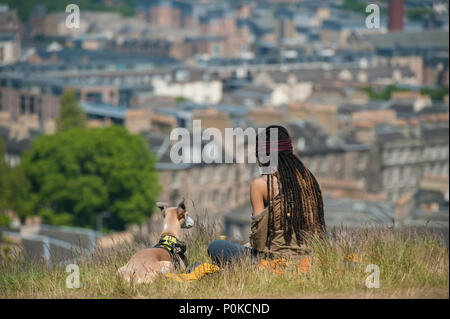 Eine sehr kühle, böhmische Mädchen sitzt in der langen Gras auf Carlton Hill an einem sonnigen Tag mit Edinburgh unter ihr und ihrem Hund Stockfoto