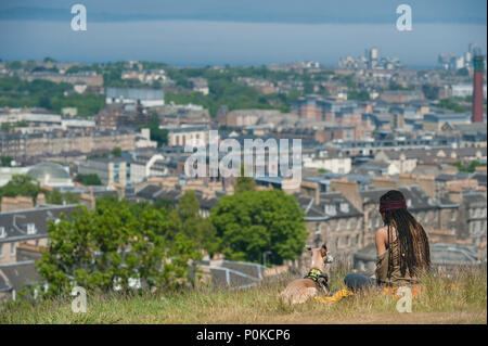 Eine sehr kühle, böhmische Mädchen sitzt in der langen Gras auf Carlton Hill an einem sonnigen Tag mit Edinburgh unter ihr und ihrem Hund Stockfoto