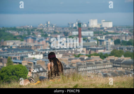 Eine sehr kühle, böhmische Mädchen sitzt in der langen Gras auf Carlton Hill an einem sonnigen Tag mit Edinburgh unter ihr und ihrem Hund Stockfoto